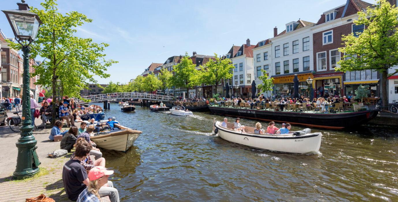 Canal with boats and people enjoying the sun and their drinks at a terrace in Leiden. 