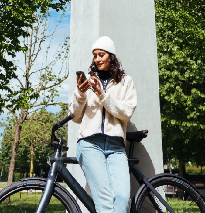 Vrouw staat buiten bij haar fiets en bekijkt de Relocation App op haar mobiele telefoon
