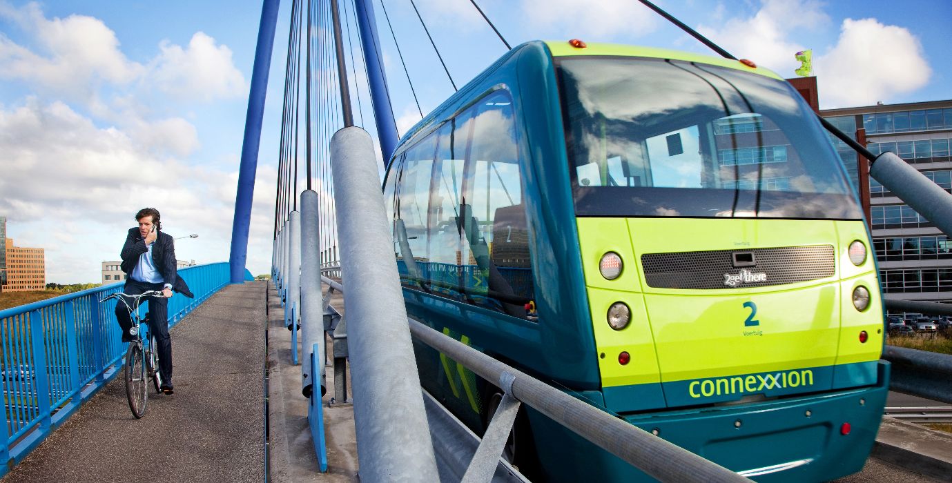 Bridge with cyclist on the left side of the road and on the right the ParkShuttle. This is an electrically-driven, autonomous shuttle service in Rotterdam.