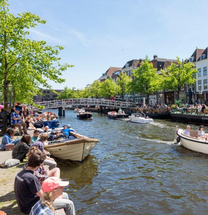 Canal with boats and people enjoying the sun and their drinks at a terrace in Leiden. 
